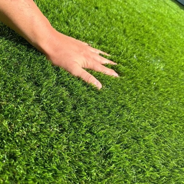 Mano colocando césped artificial en instalación realizada por GreenCare365 en Madrid